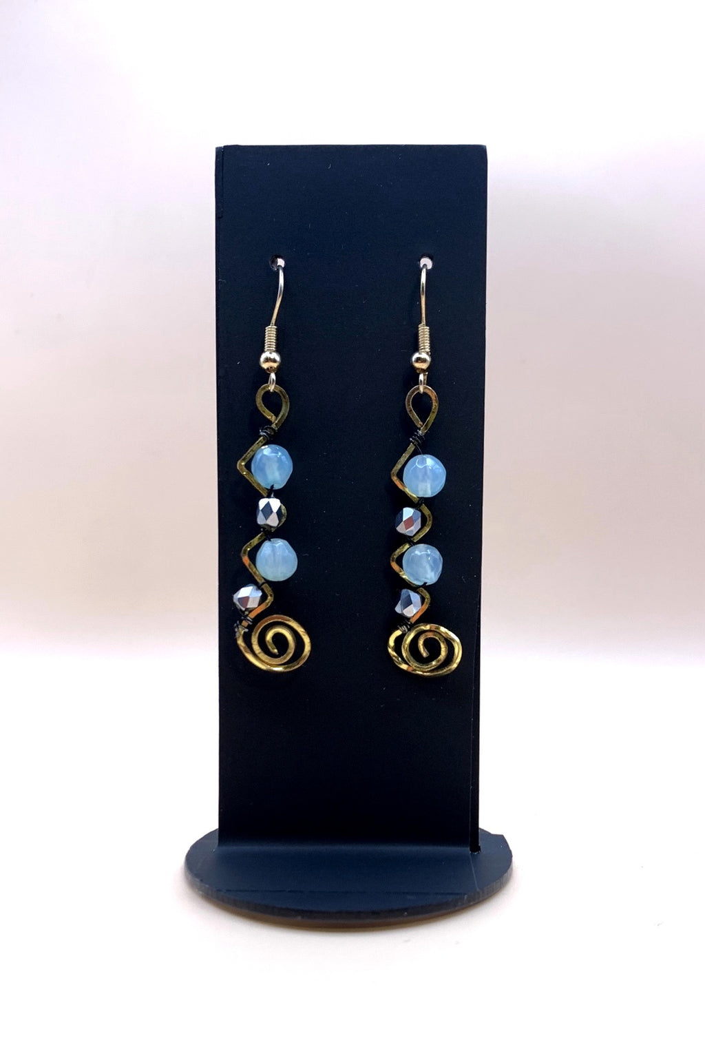 Blue and metallic bead spiral statement earrings on a black display stand