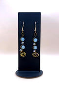 Blue and metallic bead spiral statement earrings on a black display stand