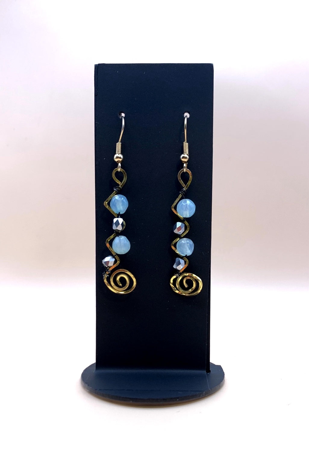Blue and metallic bead spiral statement earrings on a black display stand
